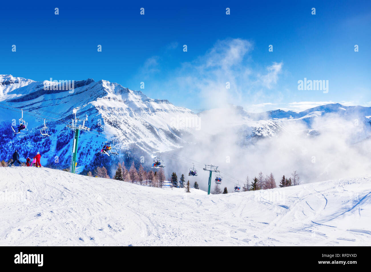 Unidentifiable skiers and snowboarders on chairlift going up a ski slope in the snowy mountain range of the Canadian Rockies. Stock Photo