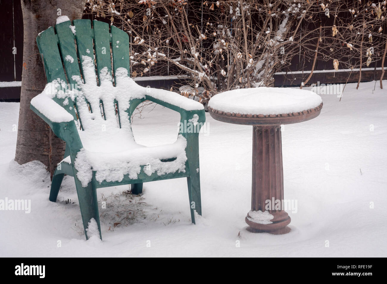 Winter is no time to sit in a cold back yard, and water will freeze in birdbath.  Snow covers all in City of Calgary, Alberta, Canada. Stock Photo