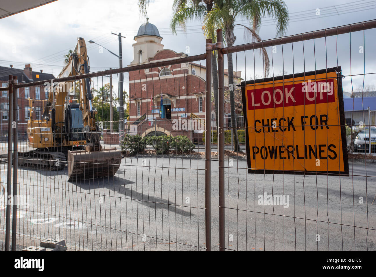 Excavator on road works behind temporary fence and warning sign Stock Photo