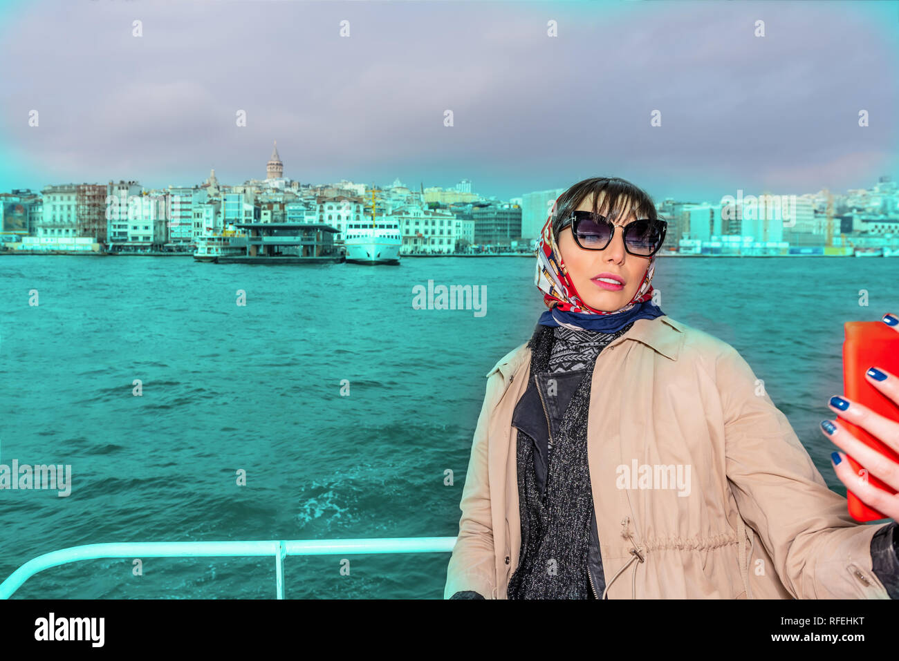 Beautiful woman take selfies while cruising in ferry with view of Galata Tower at background in Istanbul,Turkey Stock Photo