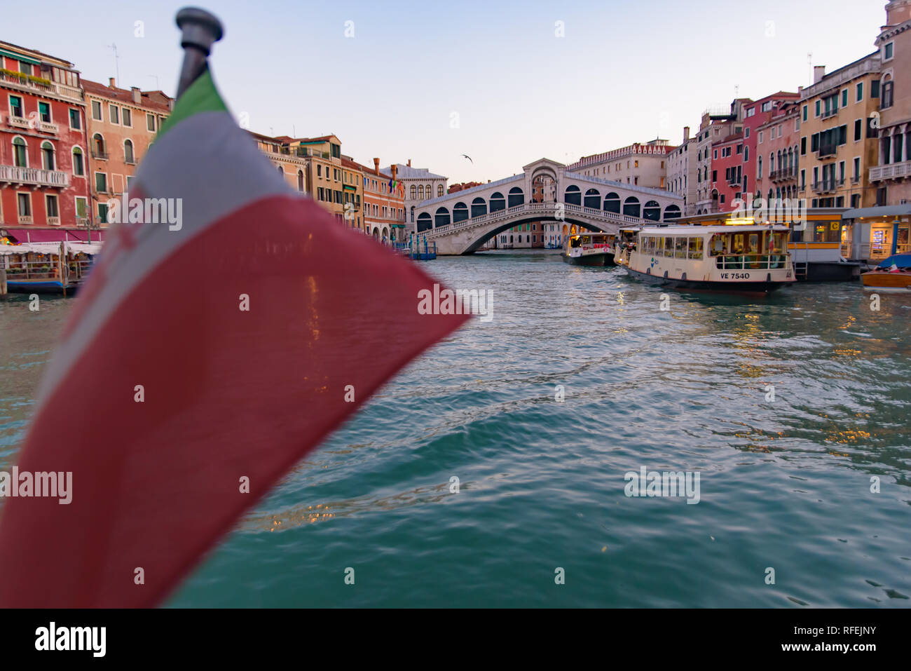 Rialto Bridge (Ponte de Rialto) across Grand Canal at sunrise / sunset time with Italian flag, Venice, Italy Stock Photo