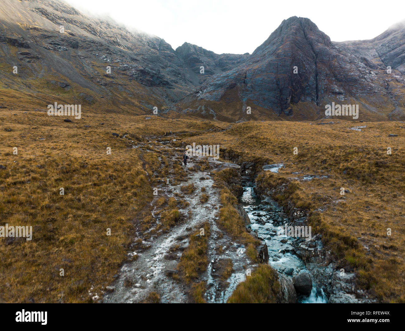 Aerial view of river streams and hiking path at the Fairy Pools with fog covered mountain background and lonely hiker (Isle of Skye, Scotland, Europe) Stock Photo