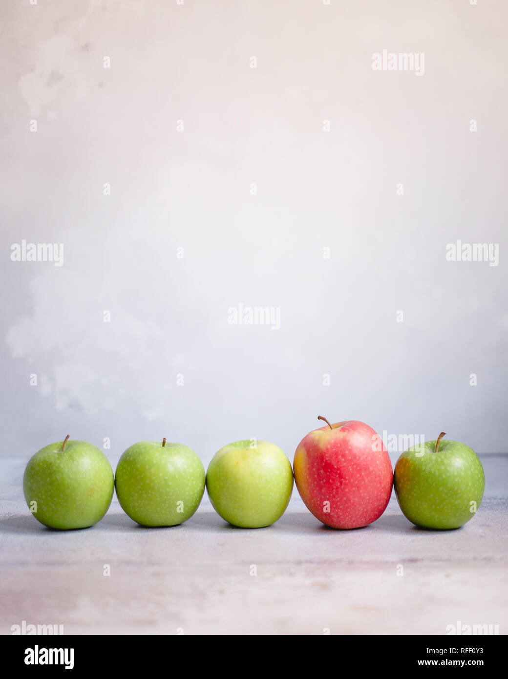 Four green apples and one red apple in a line against a neutral background Stock Photo