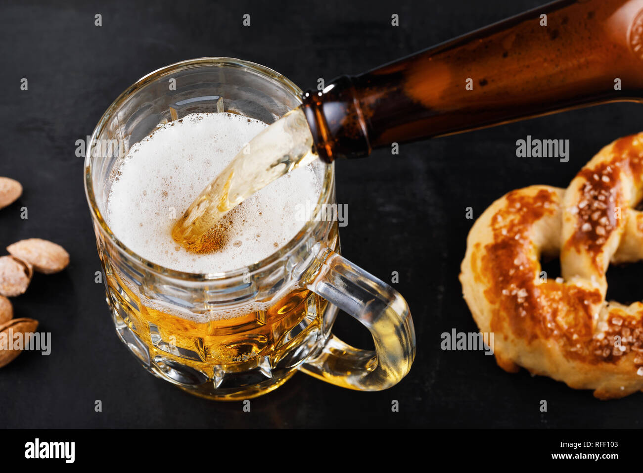 Glass of fresh light beer with salted pretzels and nuts on the table. Process of pouring the drink Stock Photo