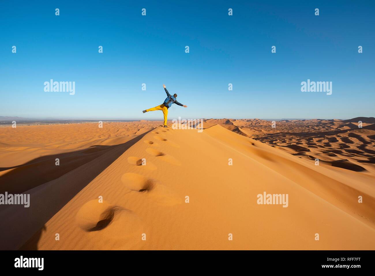 Young man on sand dune standing on one leg, Erg Chebbi, Merzouga, Sahara, Morocco Stock Photo