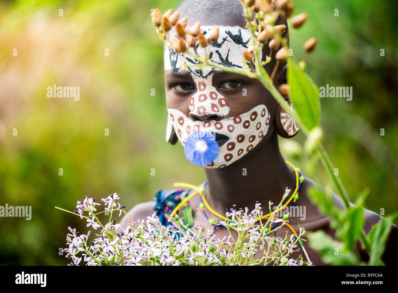 KIBISH, ETHIOPIA - AUGUST 22, 2018: unidentified woman from Surmi tribe, with  painted face and natural decorations of leave and flowers in a wreath.  Stock Photo