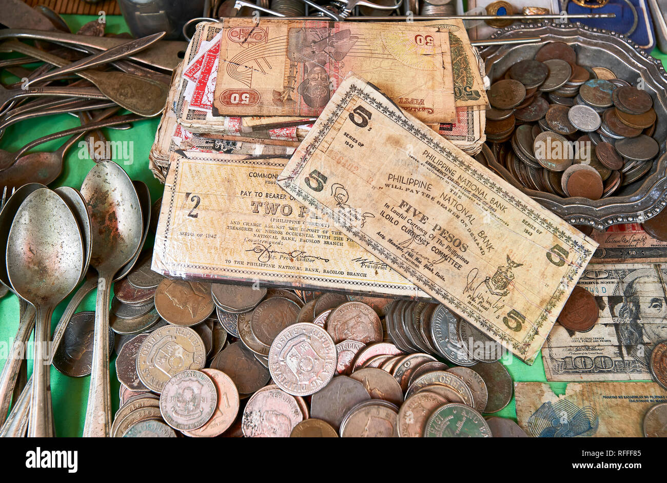 Very old Philippine bank notes and coins mixed with antique spoons on a table in a wet market in the city of Iloilo, Philippines Stock Photo