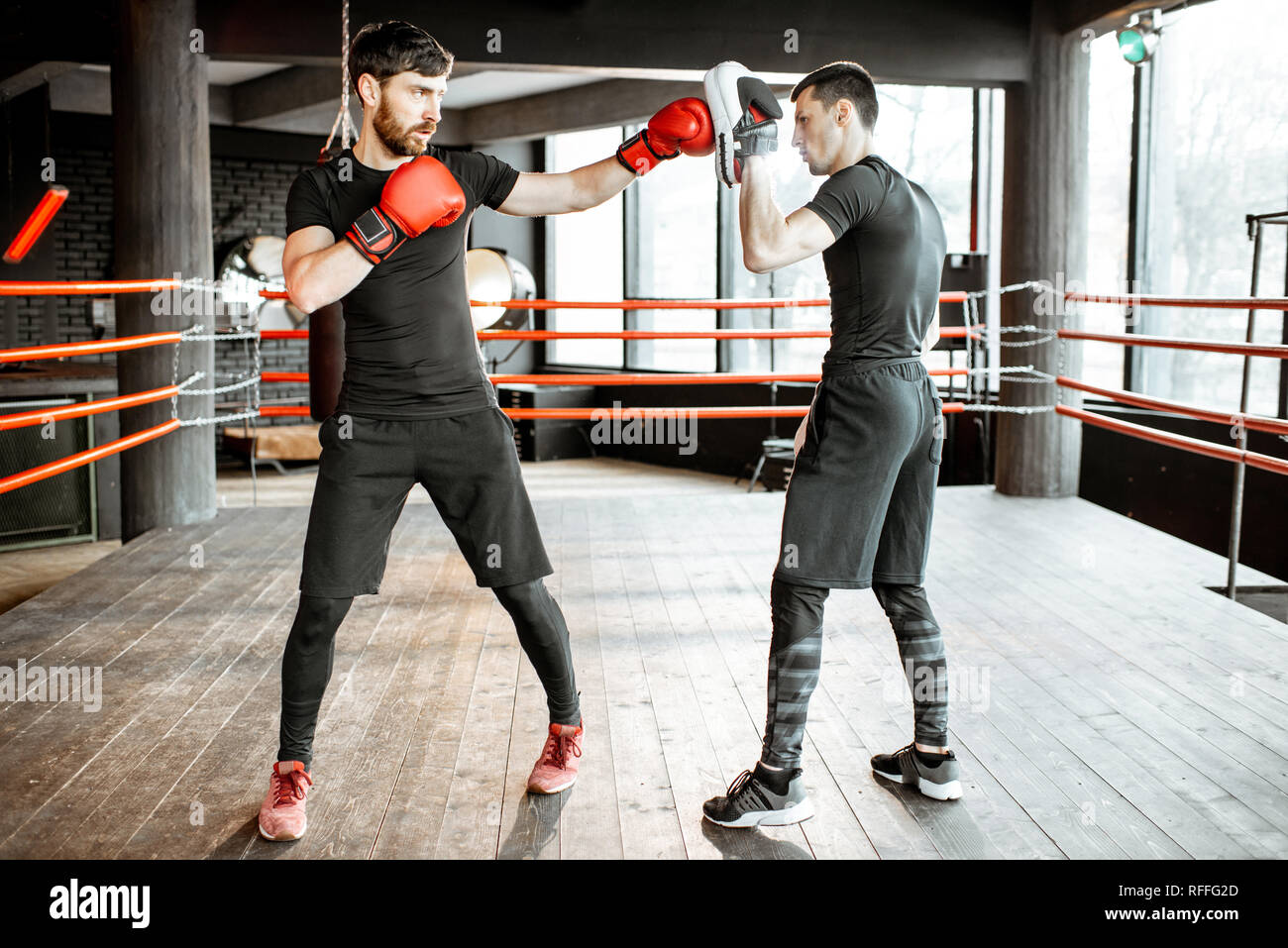 Boxing trainer showing to a man how to fight, teaching to box on the boxing ring at the gym Stock Photo
