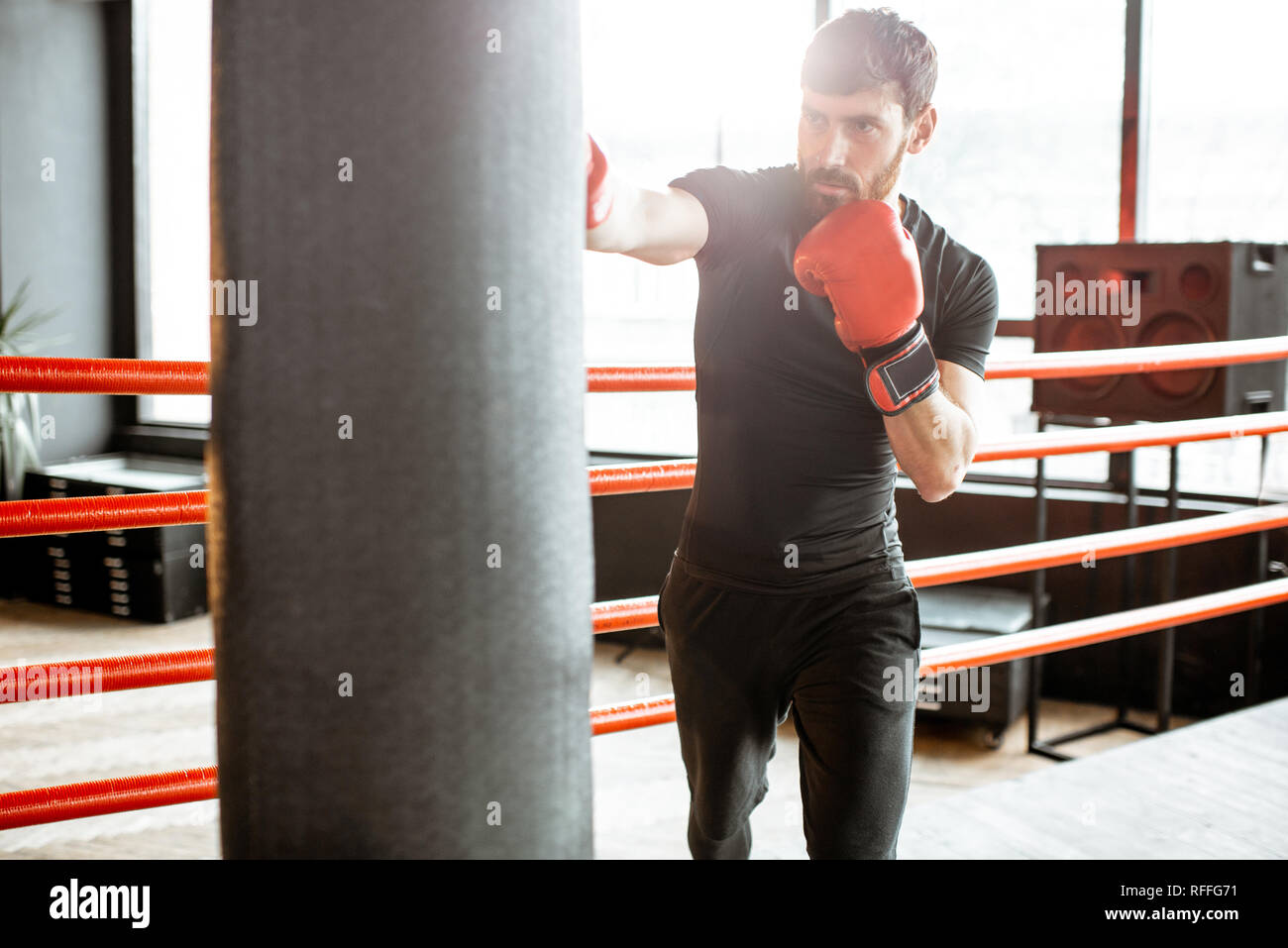 Athletic man in black sportswear training to box with punching bag on