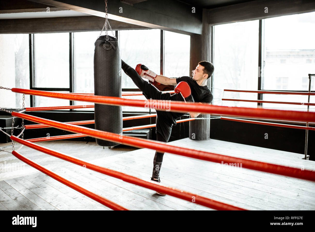 Athletic man kicking punching bag with leg, training kickboxing on the