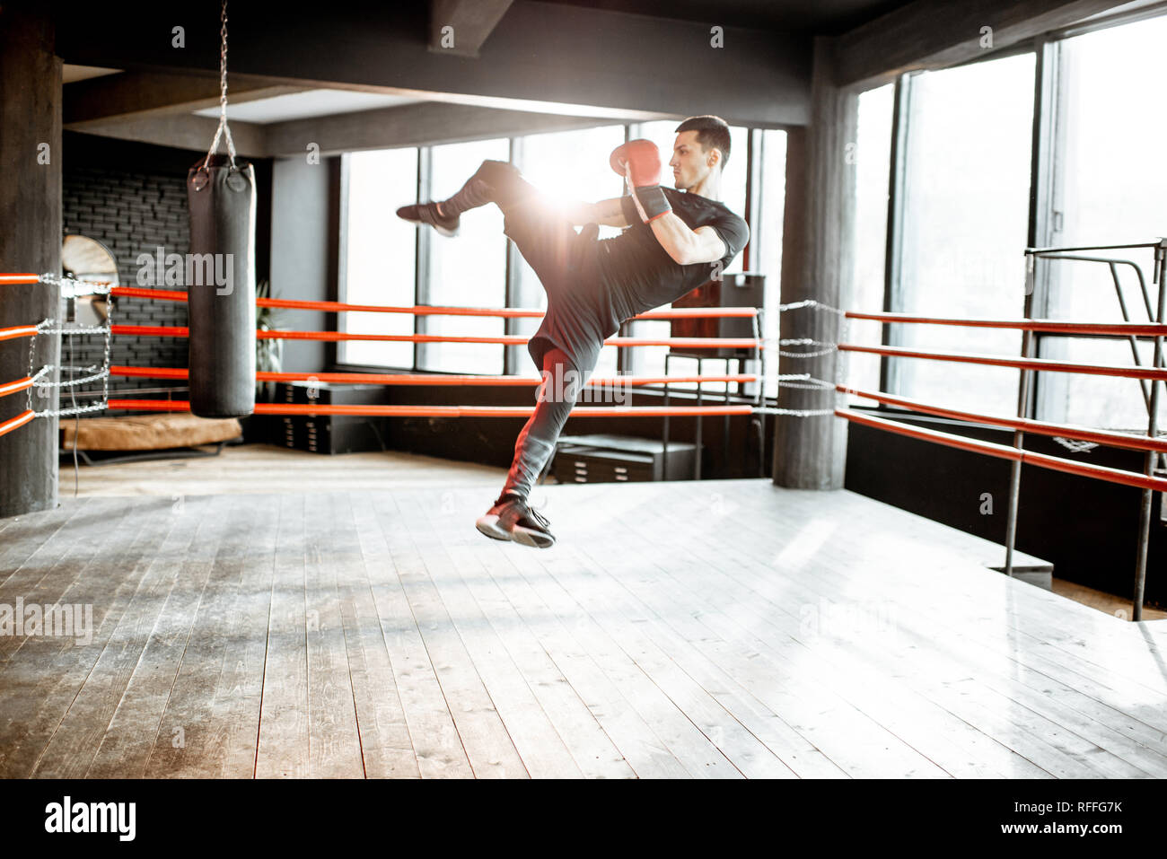 Athletic man kicking punching bag with leg, training kickboxing on the