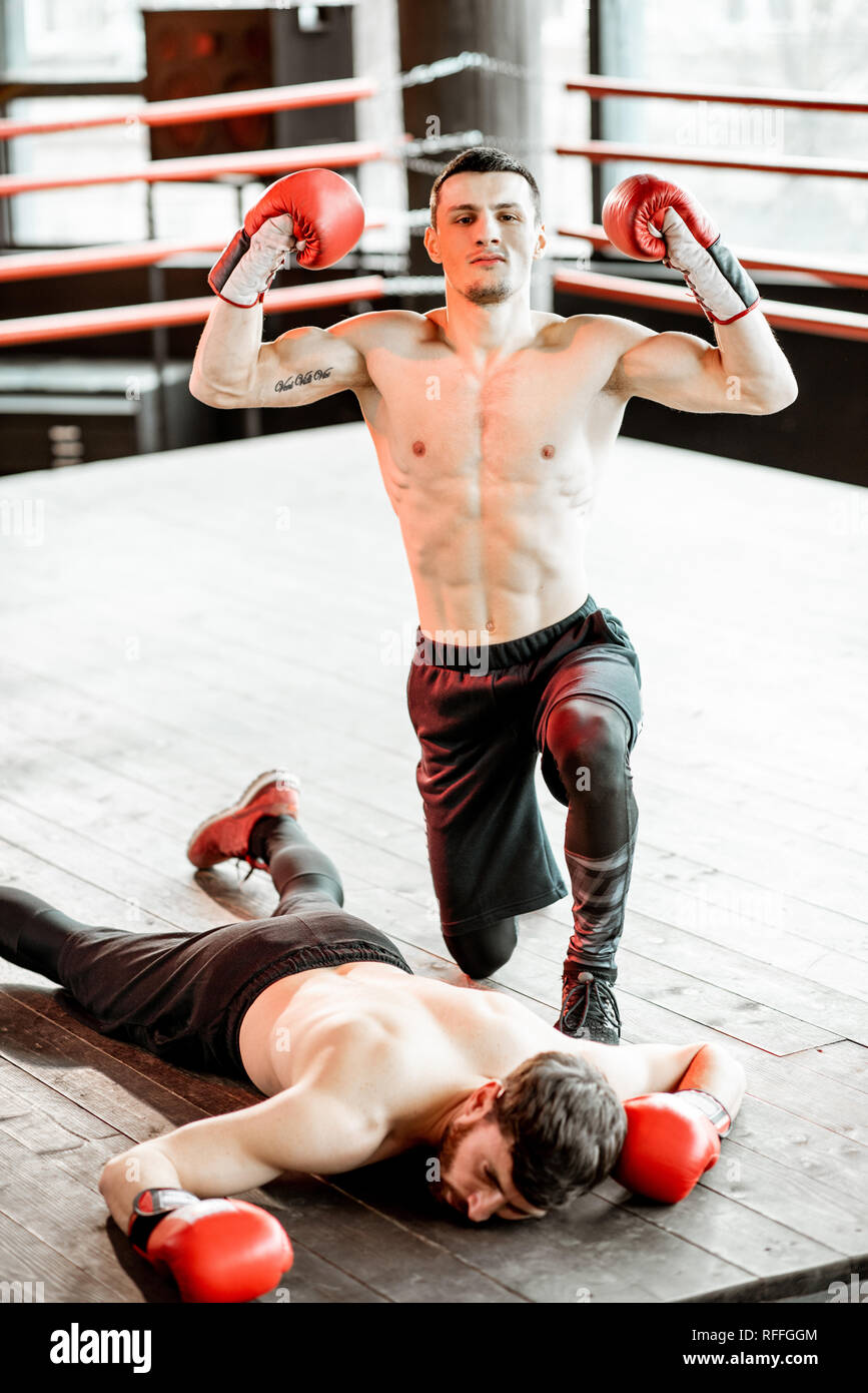 Beaten boxer lying knocked out on the boxing ring with strong man winner above Stock Photo