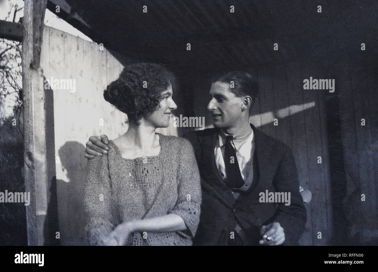 circa 1930s, historical, romantic young adult couple wearing the clothes of the era sitting in a old hut together outside looking at each other, England, UK. Stock Photo