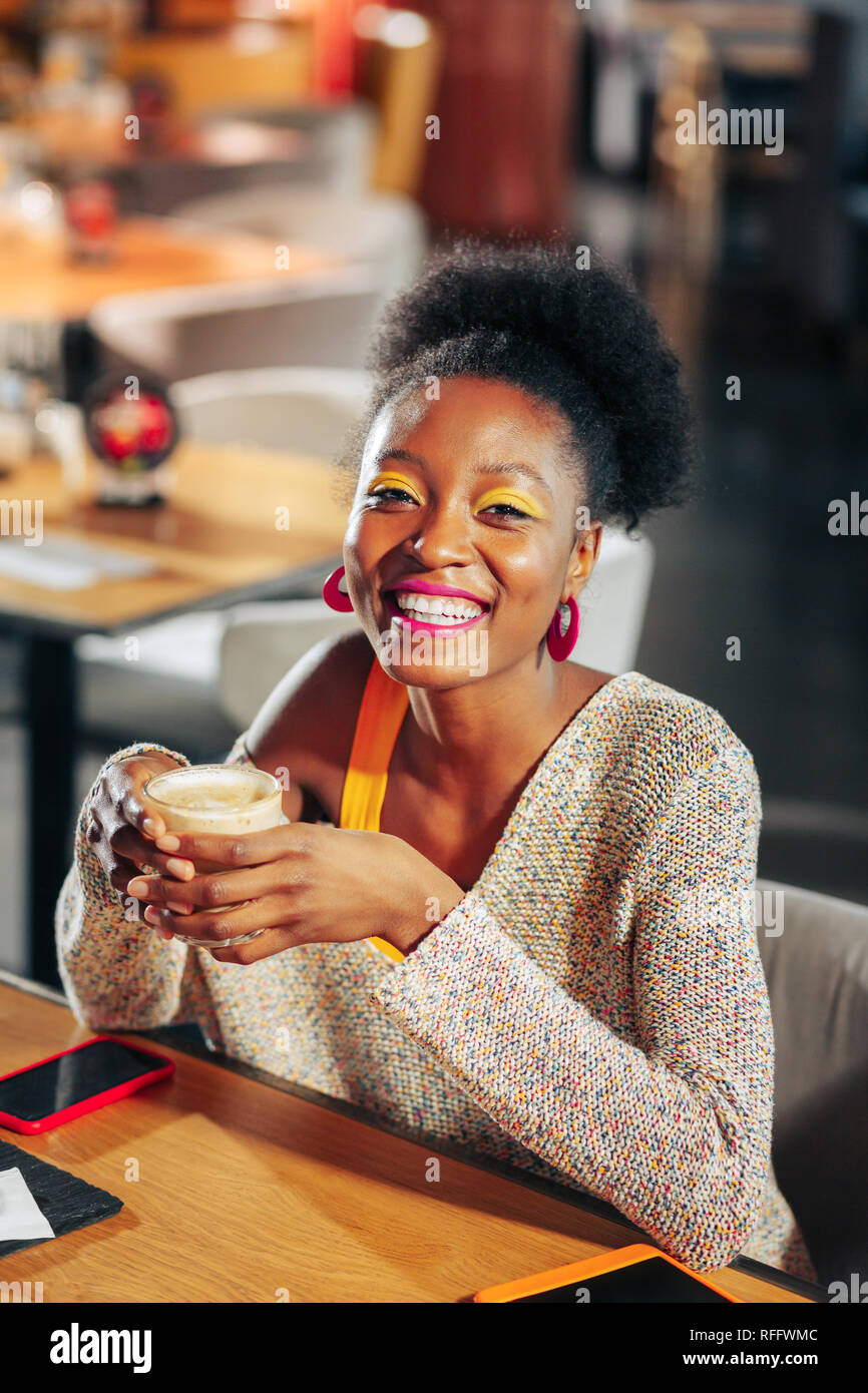 Dark-haired woman smiling broadly while enjoying coffee break Stock Photo