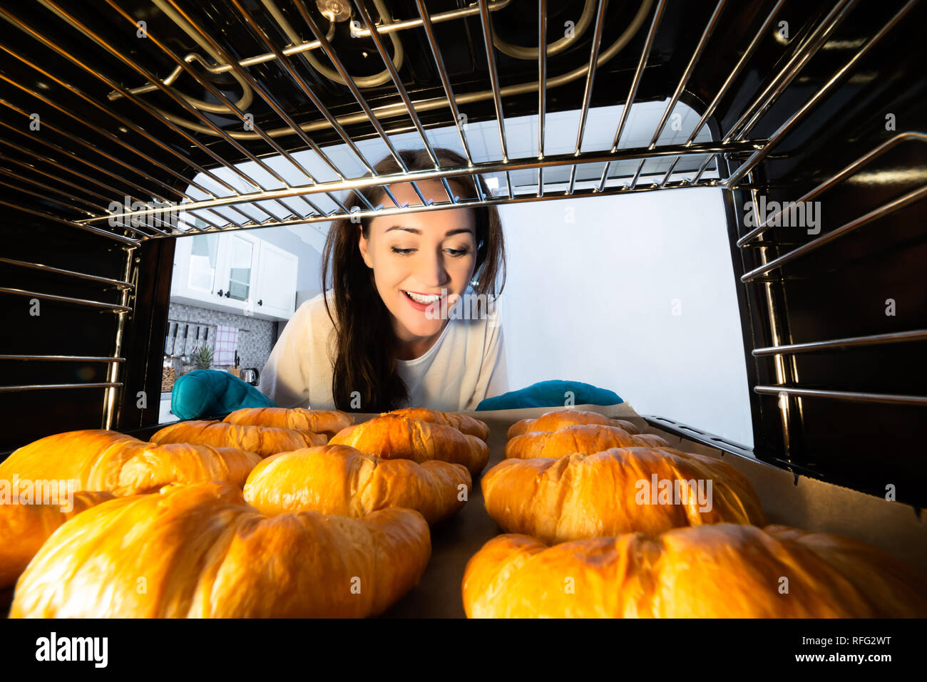 Smiling Young Woman Looking At Fresh Baked Croissants In Oven Stock Photo