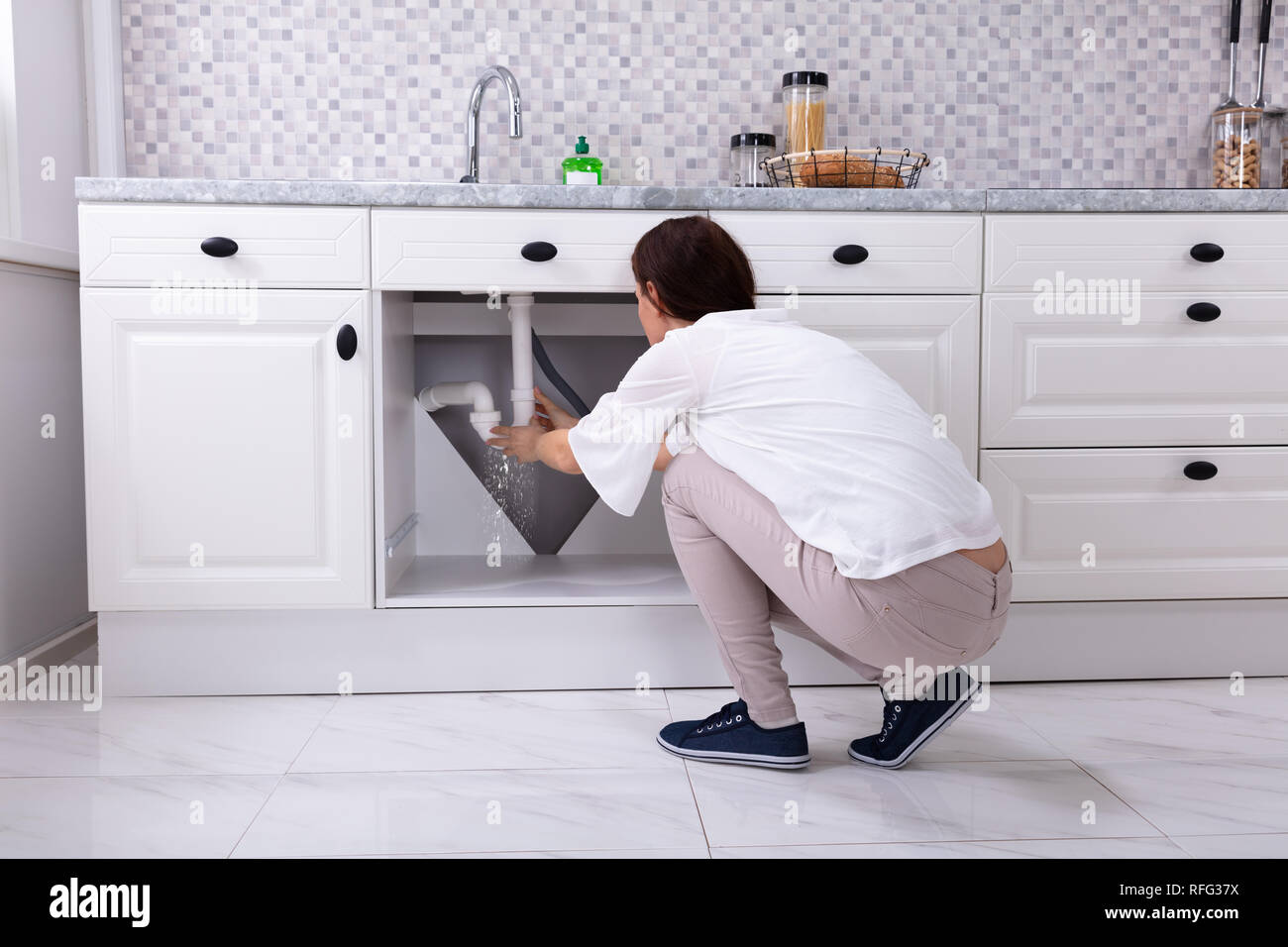 Rear View Of A Woman Trying To Stop Water Leakage From Sink Pipe In Kitchen Stock Photo Alamy