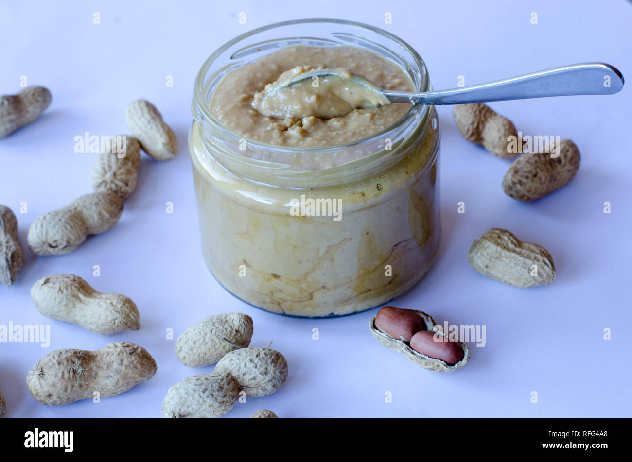 Homemade peanut butter in glass jar with peanuts spread on the table Stock Photo