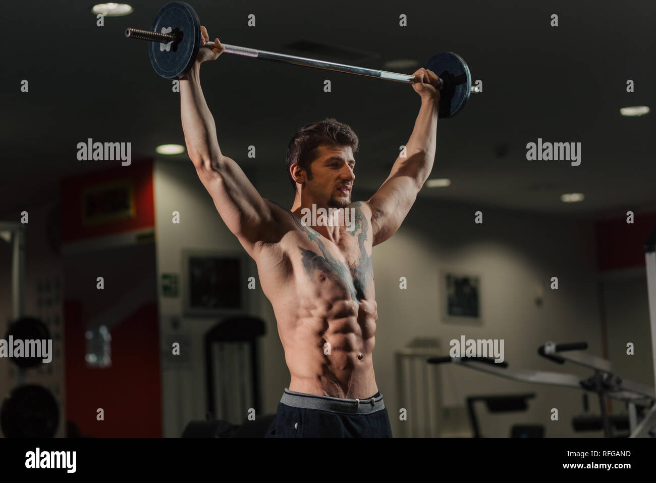 Very fit man with low body fat in the gym doing brabell shoulders exercise Stock Photo