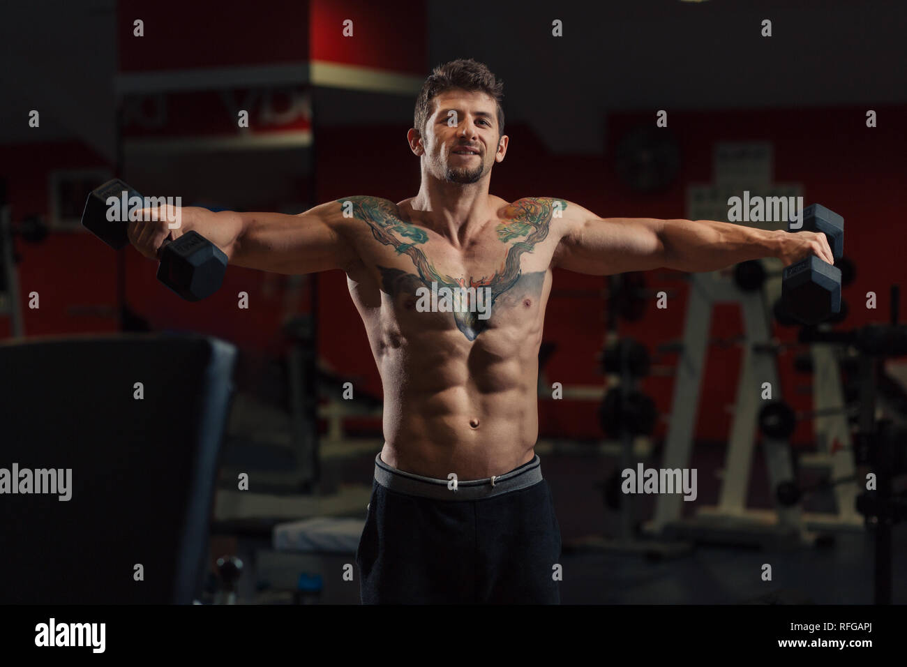Very fit man with low body fat in the gym doing dumbbell shoulders exercise Stock Photo