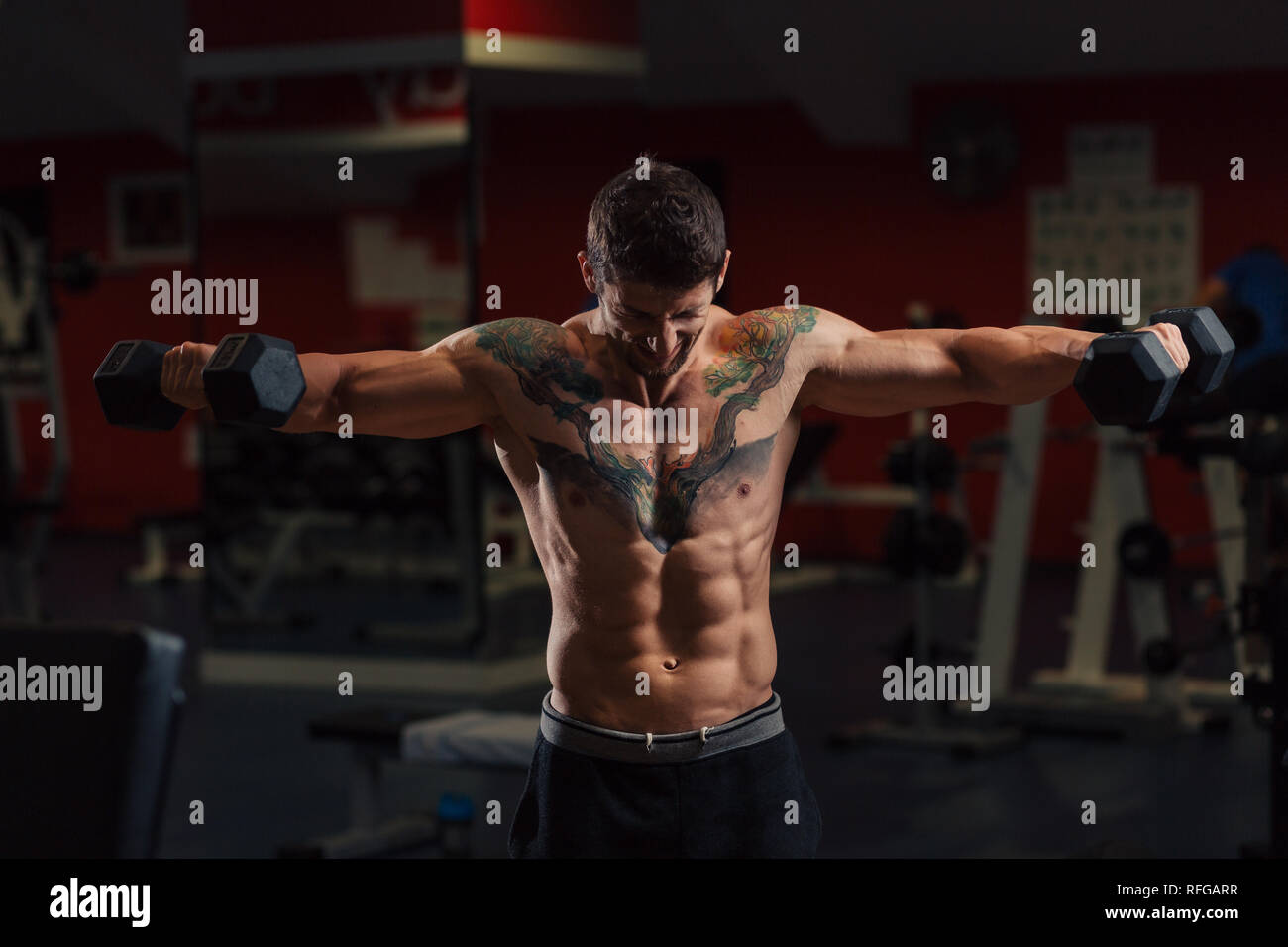 Very fit man with low body fat in the gym doing dumbbell shoulders exercise Stock Photo