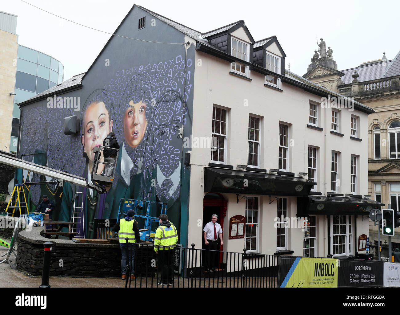 Graffiti artists work on a mural of hit TV show Derry Girls on the wall of Badgers Bar on Orchard Street in Londonderry ahead of the broadcast of the second season of the show later this year. Stock Photo