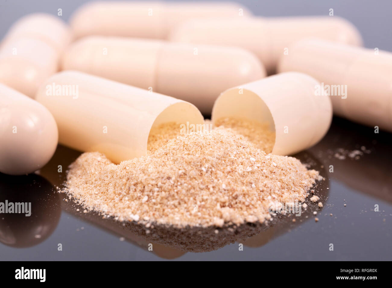 Some beige capsules and beige powder isolated on black reflective surface. Global pharmaceutical industry for billions dollars per year. Pharmaceutica Stock Photo