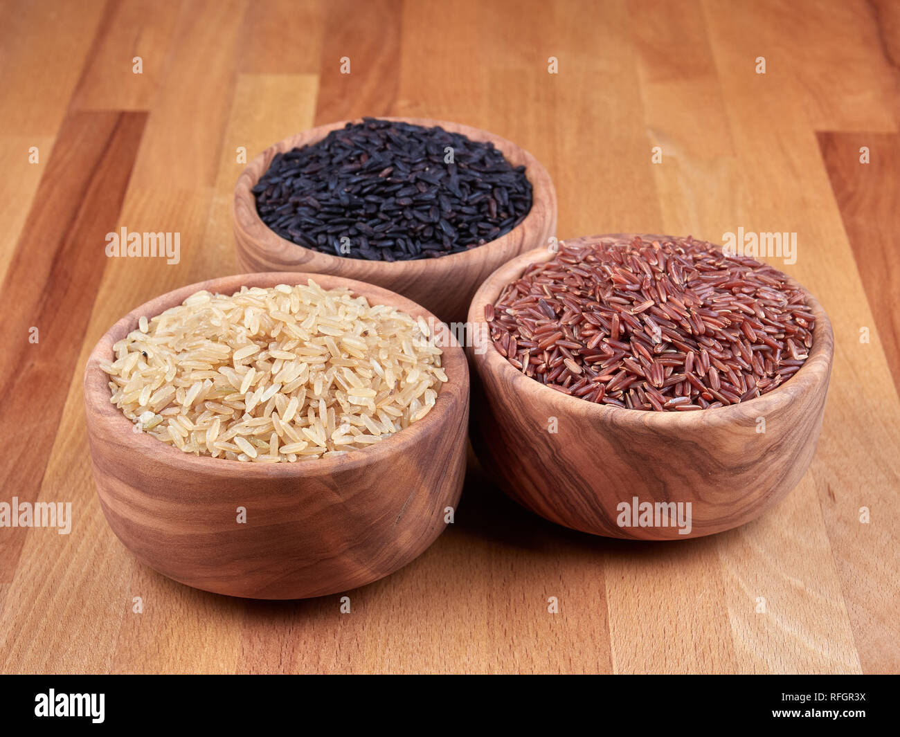 Uncooked black, red and brown rice in olive wood bowls, on a rustic wooden board Stock Photo