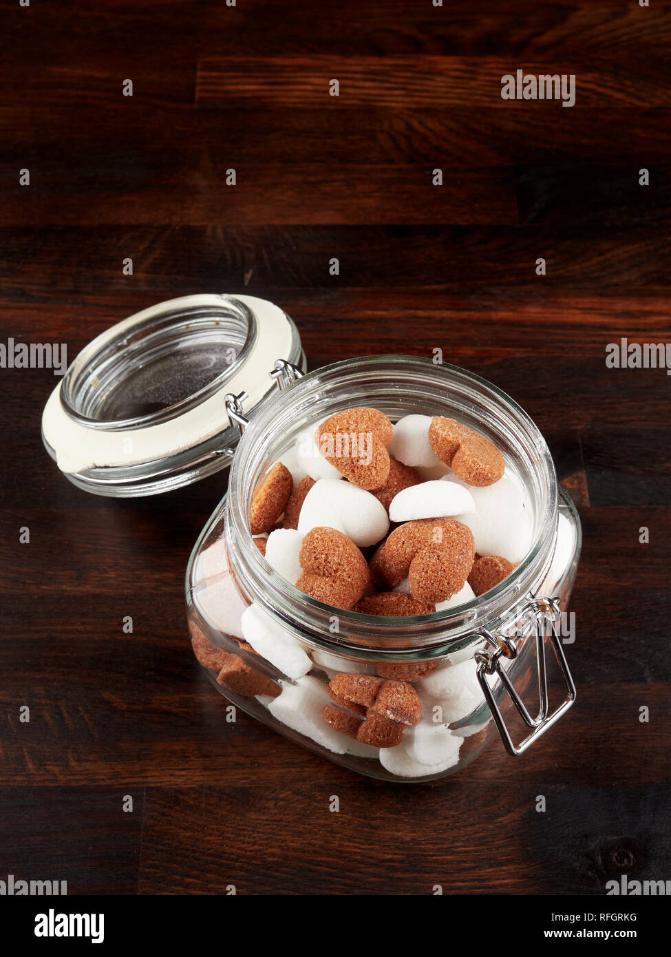 A jar filled sith white and brown heart shaped sugar cubes, on a dark wooden board Stock Photo