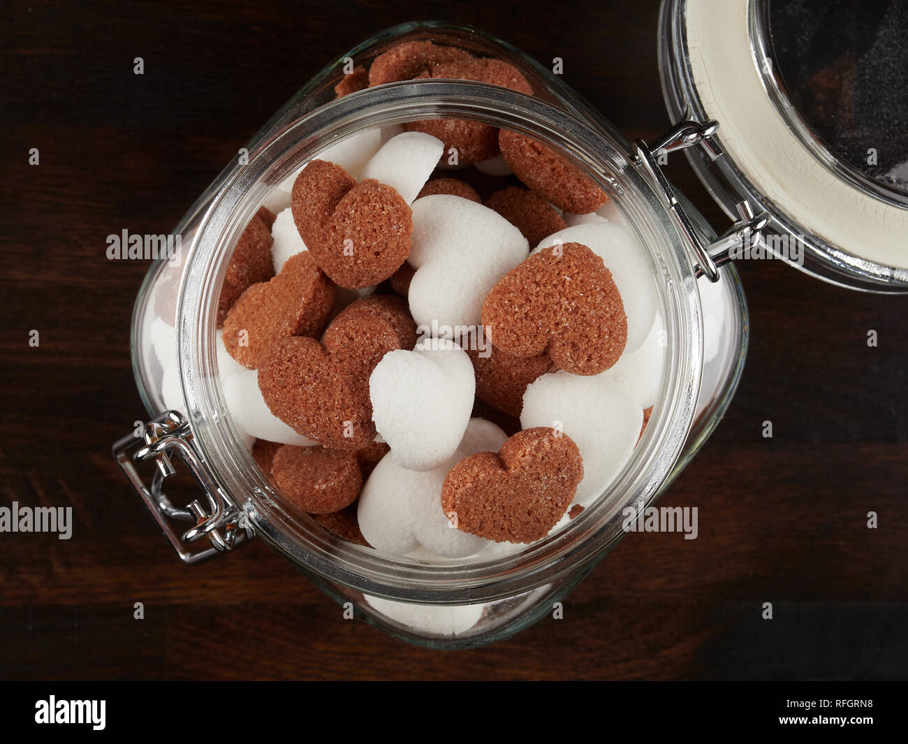A jar filled sith white and brown heart shaped sugar cubes, on a dark wooden board, flat lay Stock Photo
