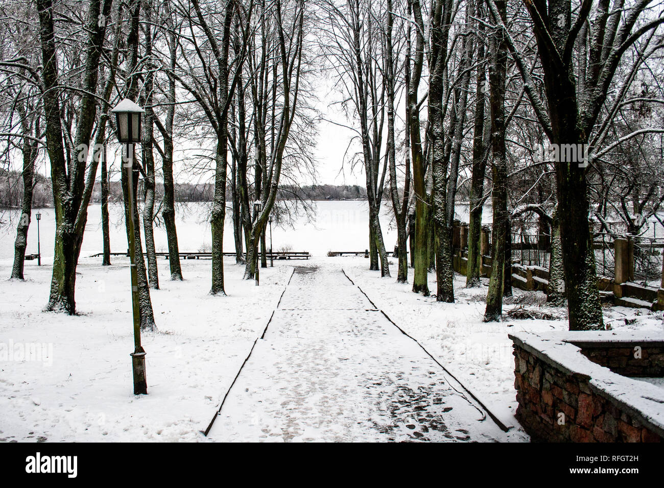 Beautiful park with old lamps, benches and lake with snow in winter ...