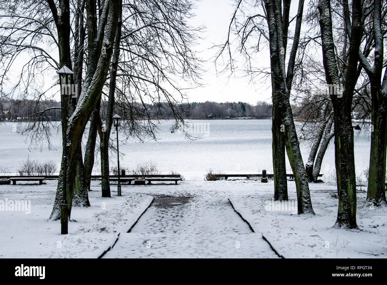Beautiful park with old lamps, benches and lake with snow in winter ...