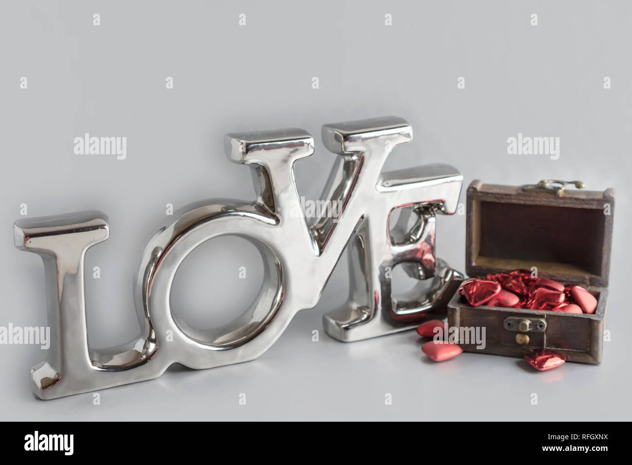 The word 'Love' with a chest of hearts.  'Love' is a chrome shiny decoration.  Chest lid open.  On a very light gray background. Stock Photo