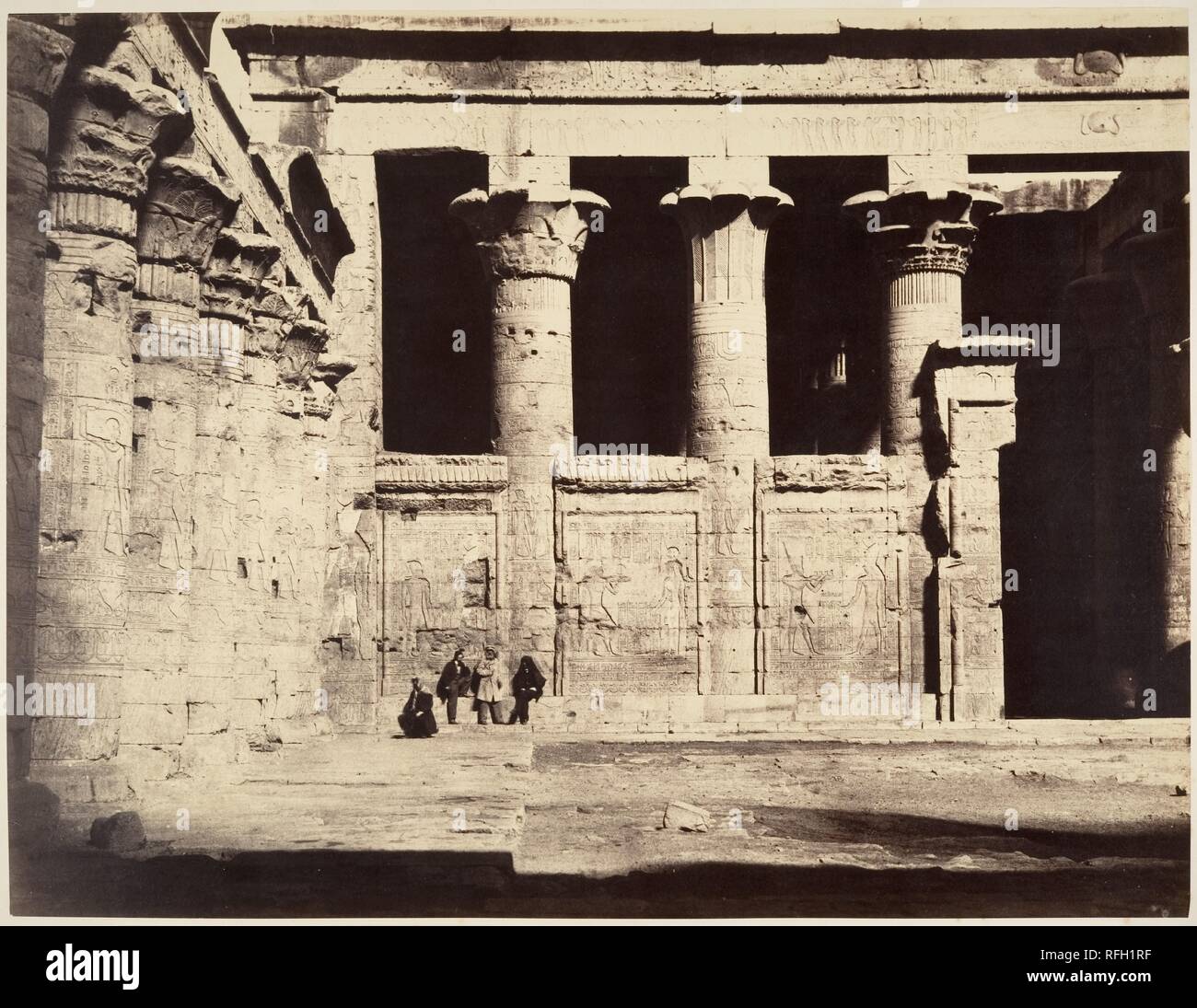 Temple of Edfu. Artist: Gustave Le Gray (French, 1820-1884). Dimensions: Image: 31.4 x 41 cm (12 3/8 x 16 1/8 in.)  Mount: 50.1 x 64.6 cm (19 3/4 x 25 7/16 in.). Date: 1867.  This photograph, taken in the great court of the Temple of Horus at Edfu, shows members of the party accompanying the sons of Egypt's viceroy Ismacil Pasha on their voyage through the country. The Temple of Edfu, built by the Ptolemy dynasty between 237 and 57 B.C., is the best preserved of all Egyptian temples. It had remained buried in the sands until it was cleared by the archaeologist Auguste Mariette in 1859. It is t Stock Photo