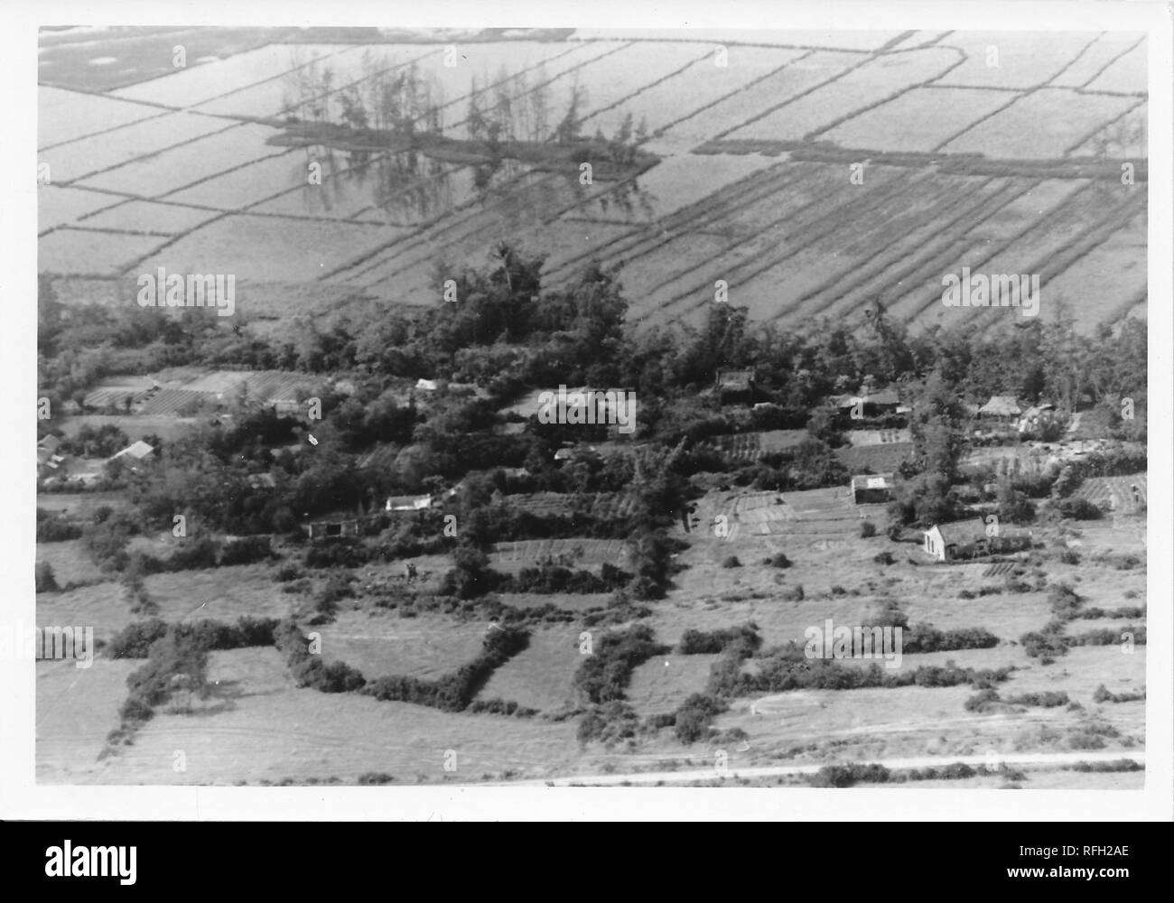 Black and white photograph, showing an aerial view or birds-eye view of a Vietnamese hamlet or small village, with flooded farmland (likely rice paddies) visible in the background, photographed during the Vietnam War, 1968. () Stock Photo