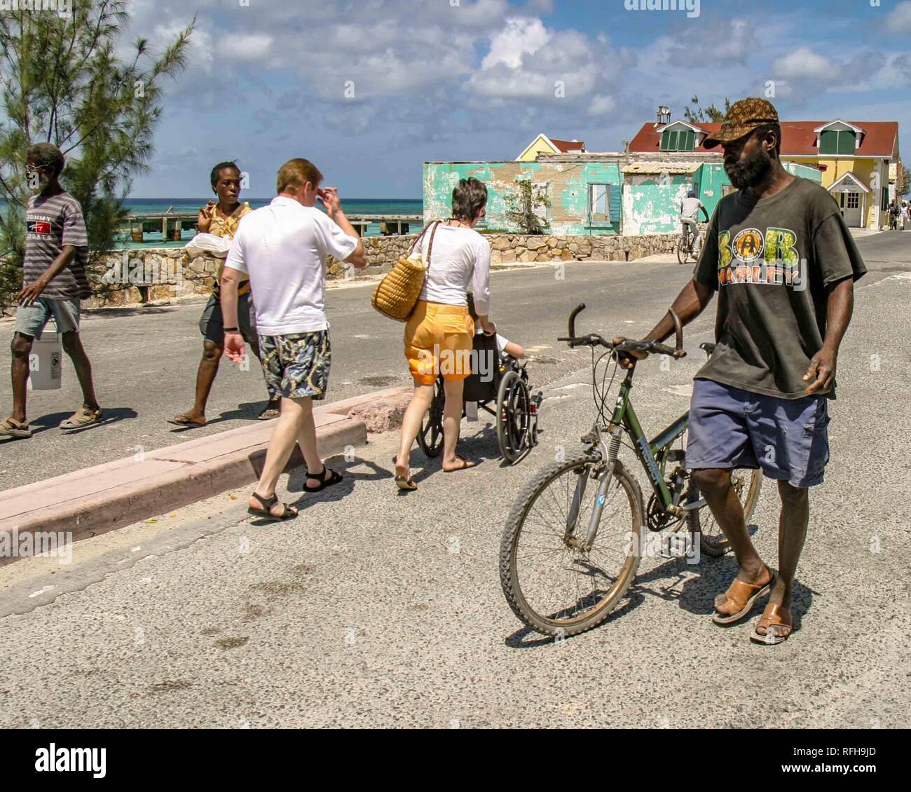 March 27, 2005 - Grand Turk Island, Turks & Caicos - A Grand Turk Island  man walks his bicycle past two tourists and some islanders on the  waterfront. The capital island of
