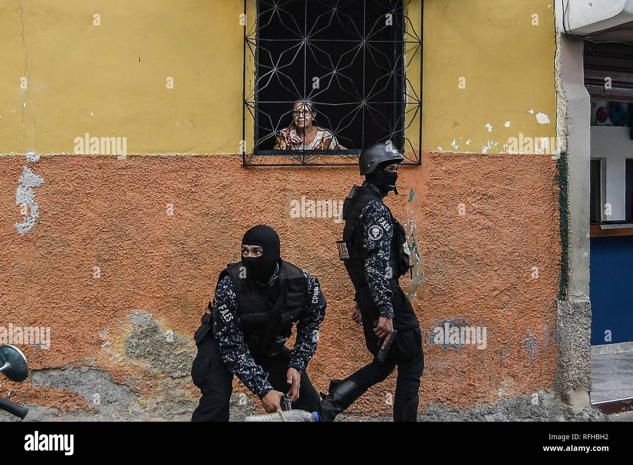 Caracas, Venezuela. 25th January 2019. Members of the Bolivarian National Police Special Forces (‘FAES’ in Spanish) seen taking position while an old woman look at them through her window during a Police raid operation against criminal groups at Petare slum in Caracas. Credit: SOPA Images Limited/Alamy Live News Stock Photo