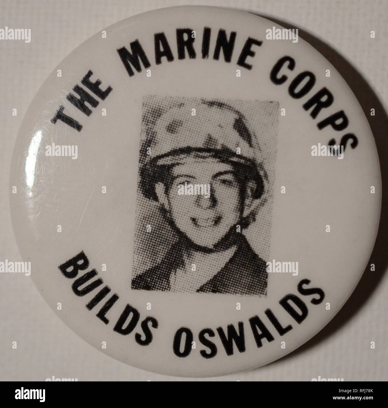 Black and white anti-war pin or button with a headshot of President John F Kennedy's assassinator, Lee Harvey Oswald, wearing a helmet and uniform, and smiling at the camera, during his posting with the United States Marine Corps, encircled by the text 'The Marine Corps Builds Oswalds', issued during the Vietnam War, 1965. () Stock Photo