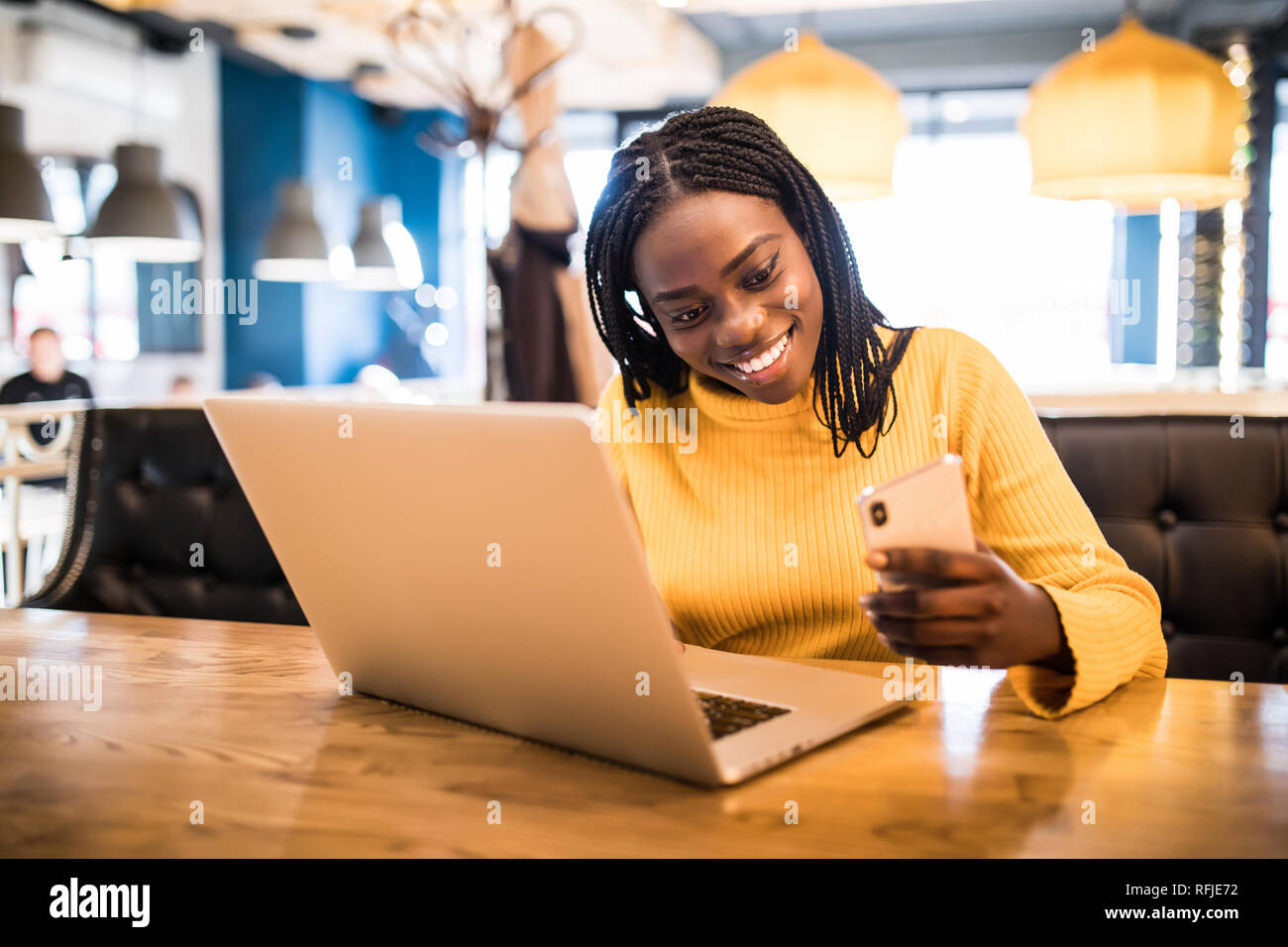 Portrait of happy young african woman in a coffee shop using mobile ...