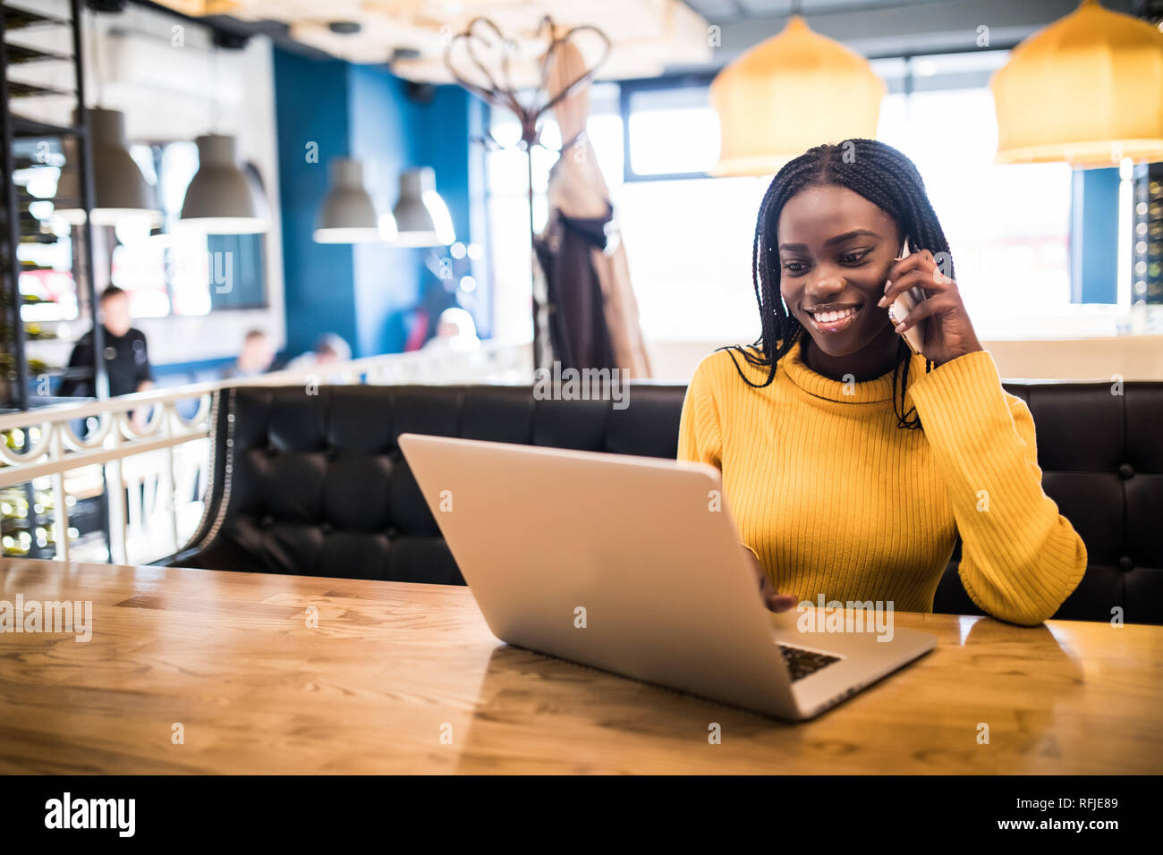 Closeup portrait of young african woman relaxing in cafe with laptop and making phone call Stock Photo