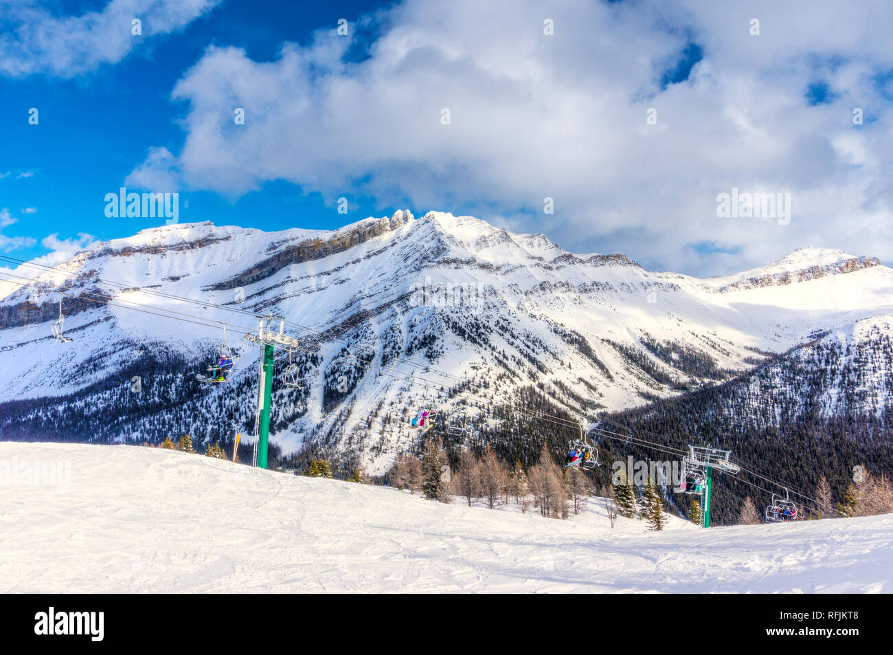 Unidentifiable skiers and snowboarders on chairlift going up a ski slope in the snowy mountain range of the Canadian Rockies. Stock Photo