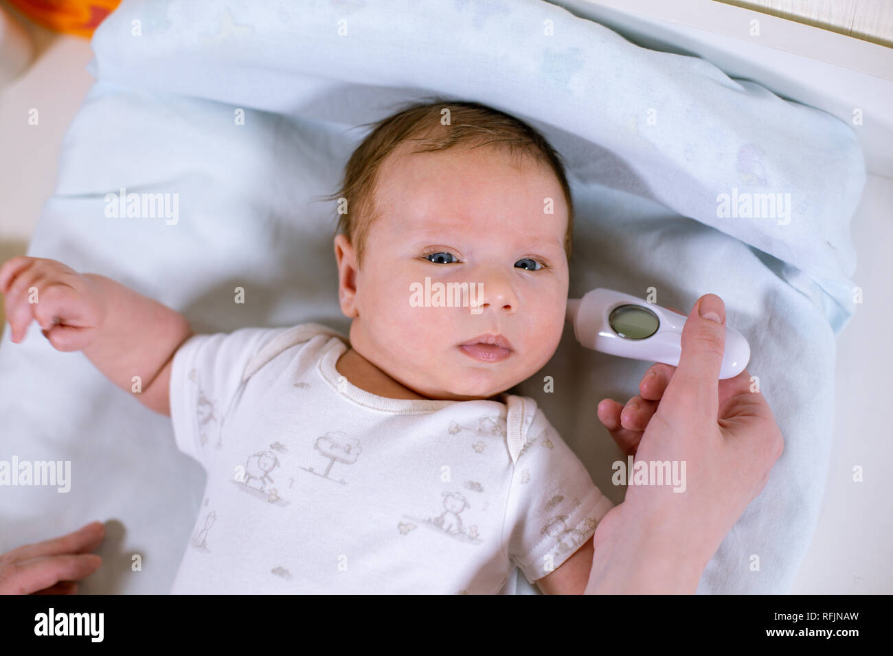 Measuring baby's temperature with contactless thermometer. Mom measures the baby's body temperature with a thermometer in the ear Stock Photo