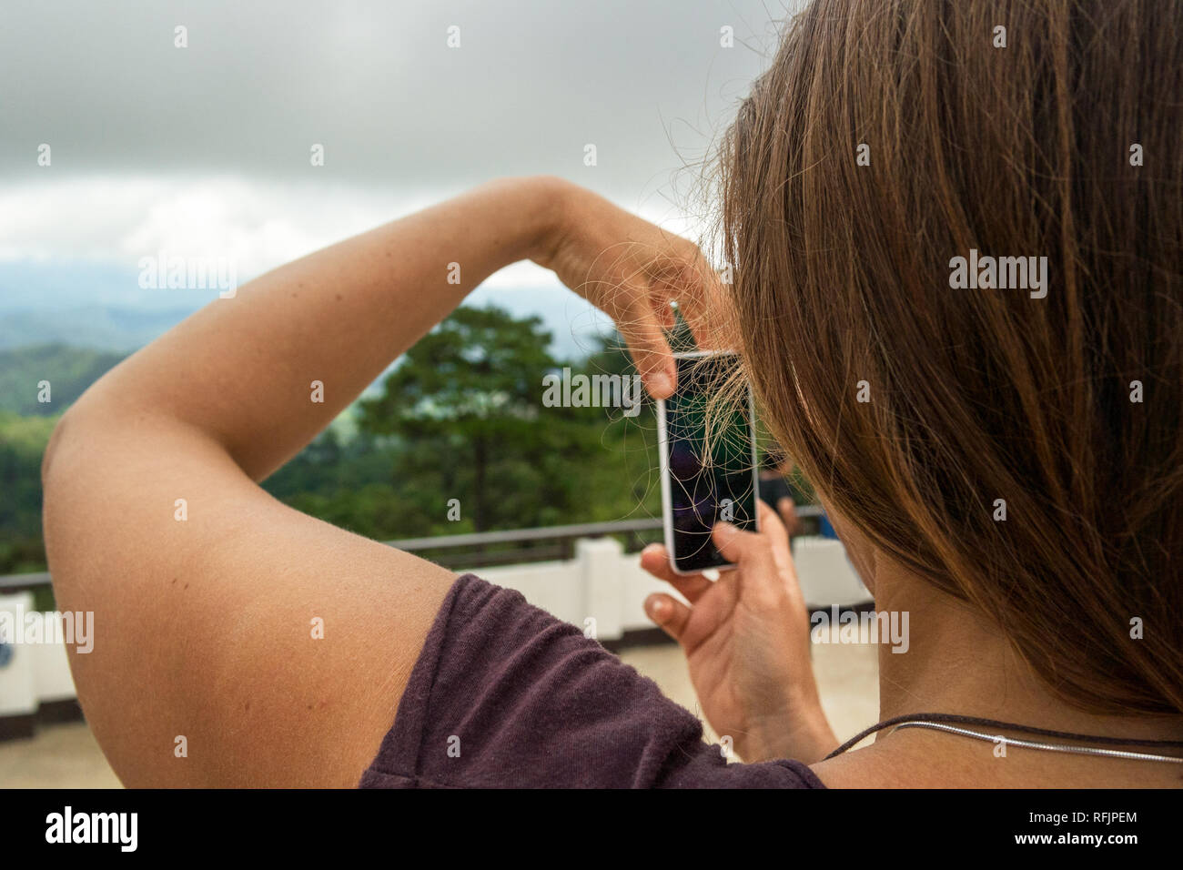 A young woman with brown hair use here smart phone to take a photo of the surrounding green landscape. Stock Photo