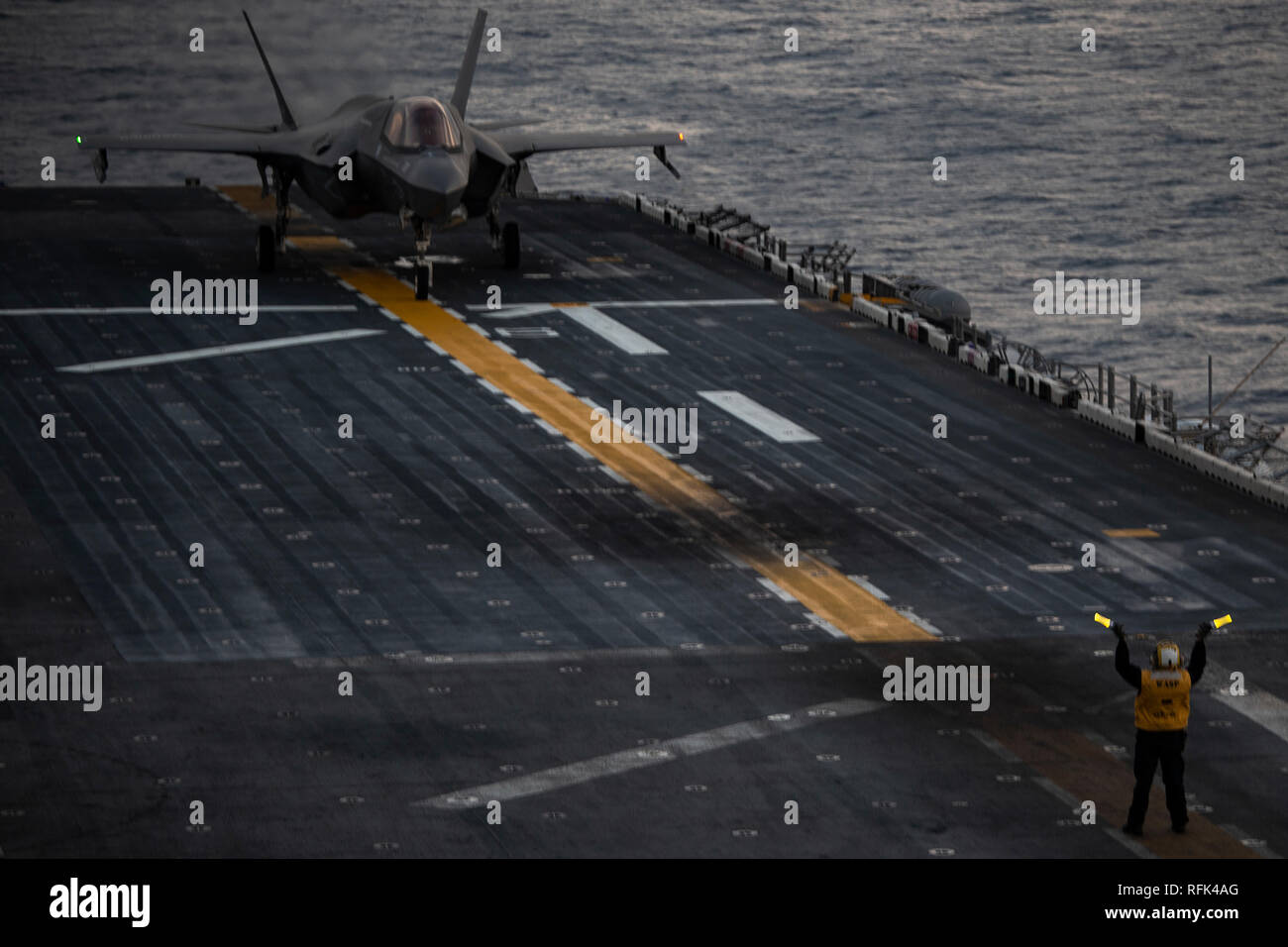 A U.S. Navy aviation boatswain’s mate assigned to the amphibious assault ship USS Wasp (LHD 1) signals an F-35B Lightning II aircraft with Marine Fighter Attack Squadron (VMFA) 121 during flight operations while underway in the East China Sea, Jan. 24, 2019. Aviation boatswain’s mates wear distinctive, bright yellow shirts and use a variety of hand and arm signals to communicate with naval aviators and deck crew during flight operations. Marine Medium Tiltrotor Squadron (VMM) 262 (Reinforced) and VMFA-121 comprise the Aviation Combat Element for the 31st Marine Expeditionary Unit (MEU). Its na Stock Photo