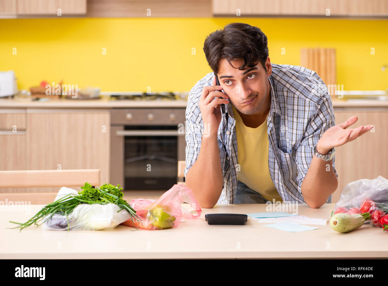 Young man calculating expences for vegetables in kitchen Stock Photo
