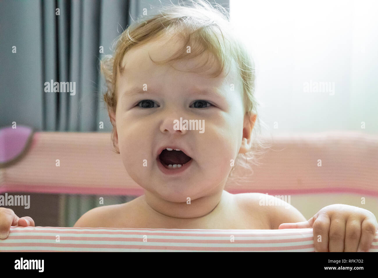 Cute laughing baby standing in a pink bed. Pink nursery for small