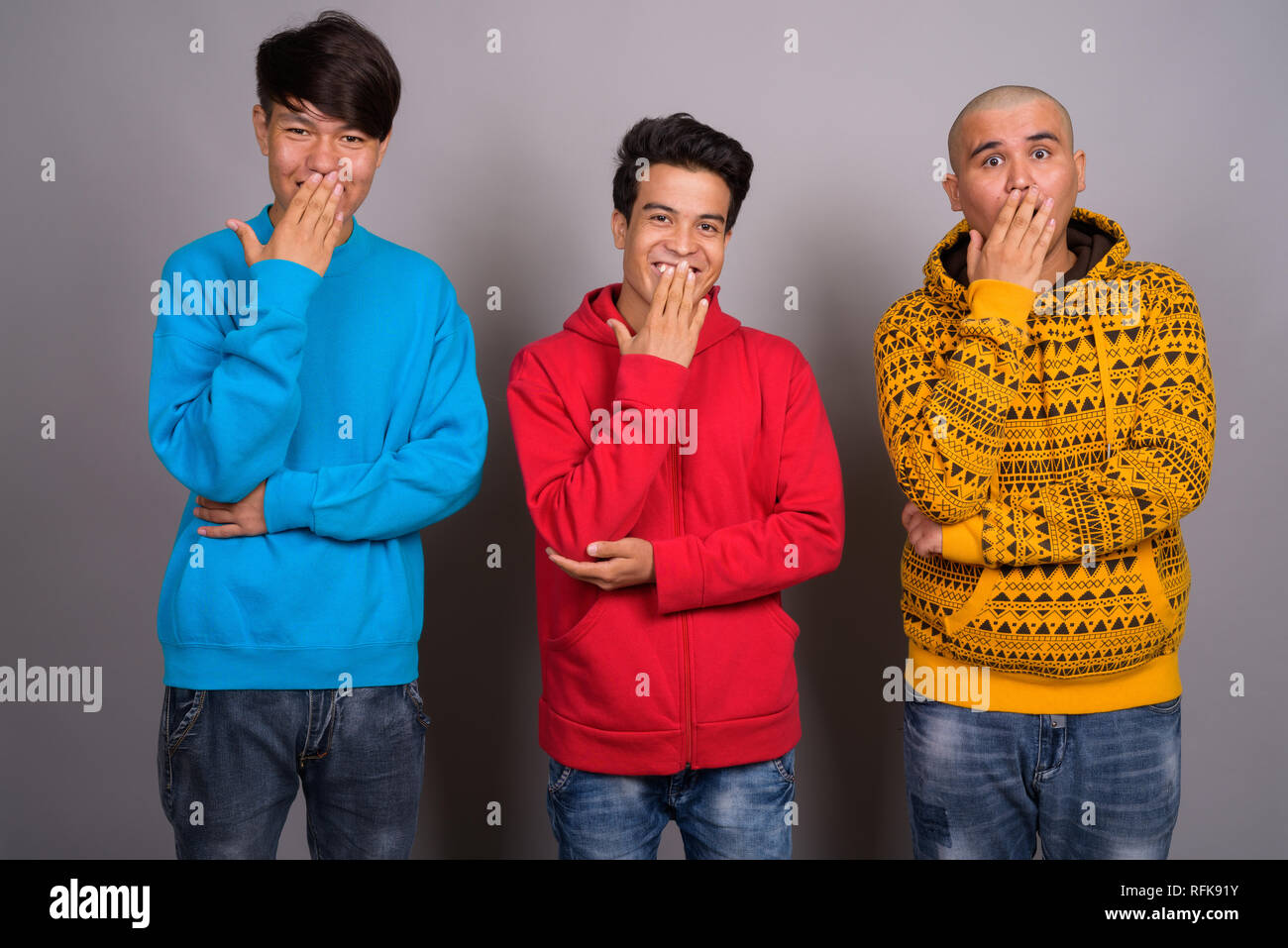 Three young Asian men wearing warm clothing against gray backgro Stock Photo