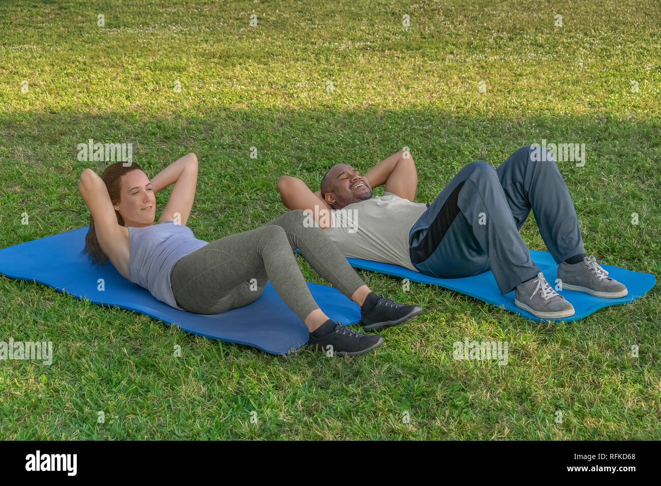 They start by doing situps on yoga mats on the grass as part of the exercise routine. Healthy living is important to a modern couple. Stock Photo