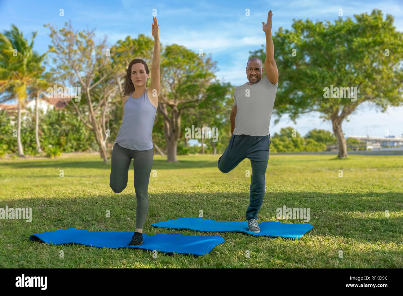 They start by standing on one leg holding the other back and reaching up high with the other hand to balance themselves on yoga mats exercising. Stock Photo