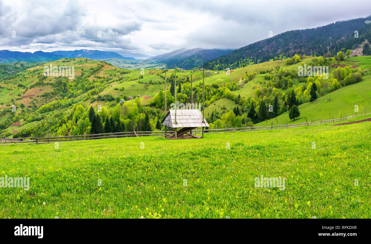 hay shed on a grassy field in mountains. beautiful countryside landscape in springtime. cloudy forenoon. village on the distant hills Stock Photo