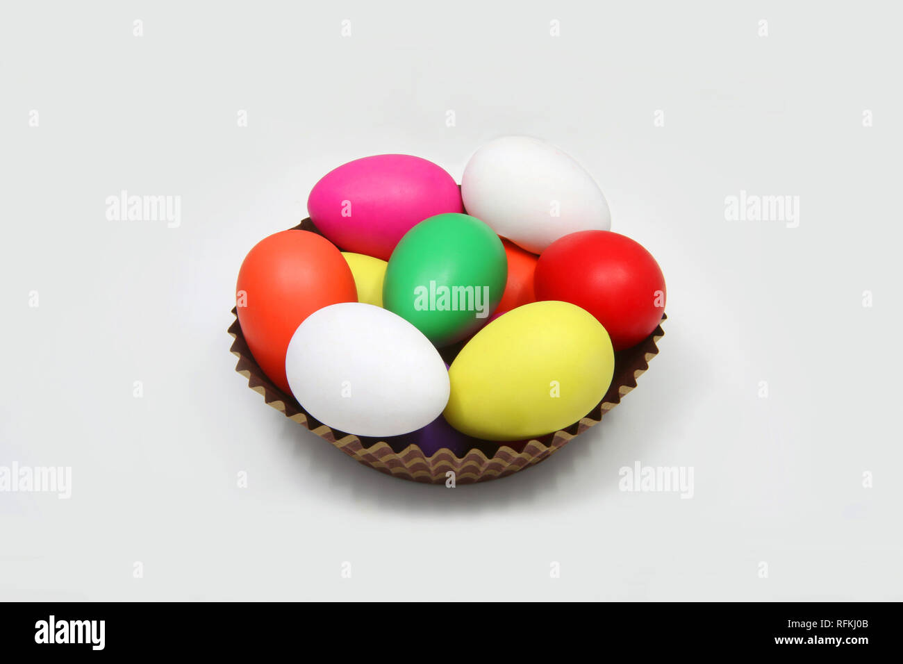 Multi colored easter eggs in a brown basket against a white background. Stock Photo